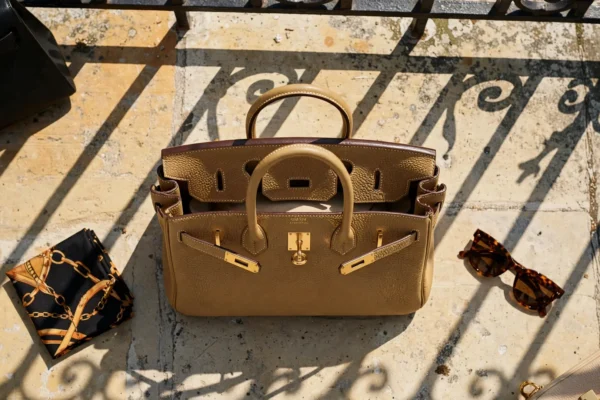 Bolso Hermès Birkin de piel togo dorada en una terraza de piedra caliza al mediodía, con sombras duras
